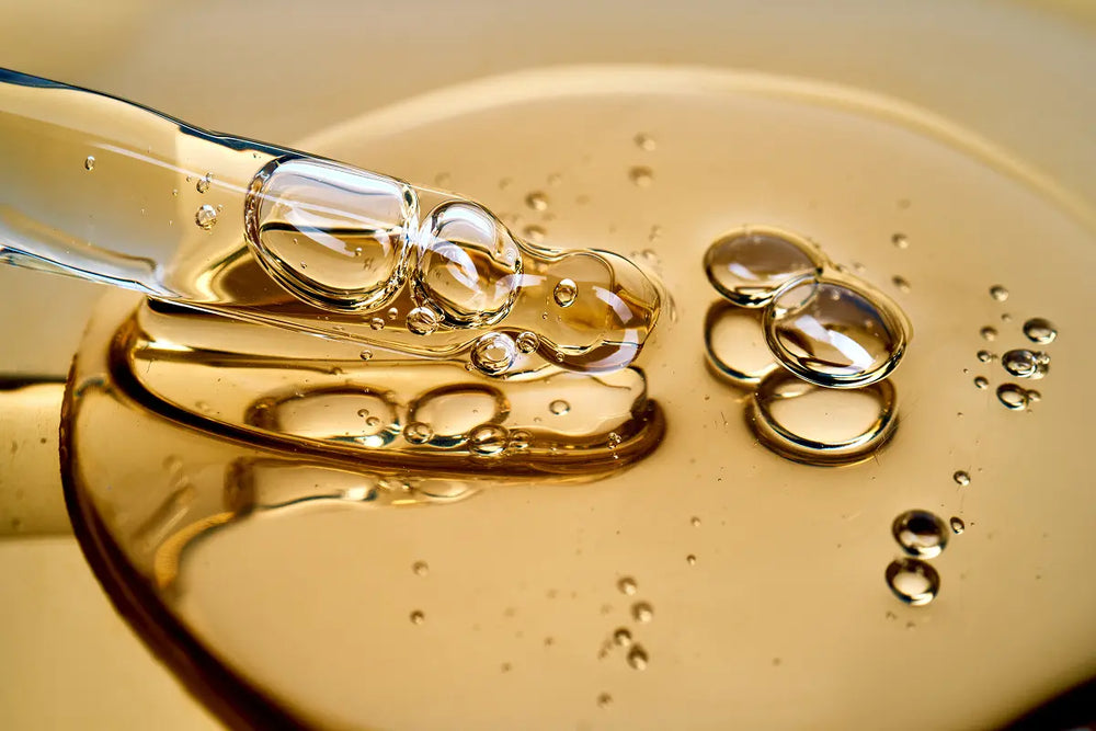 Macro view of clear serum being dispensed from a glass pipette into a golden gel, with fine bubbles suspended throughout