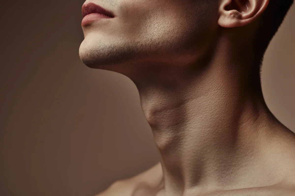 Close-up profile view of a man's jawline and neck against a warm neutral backdrop, showing the angle where the jaw meets the neck.