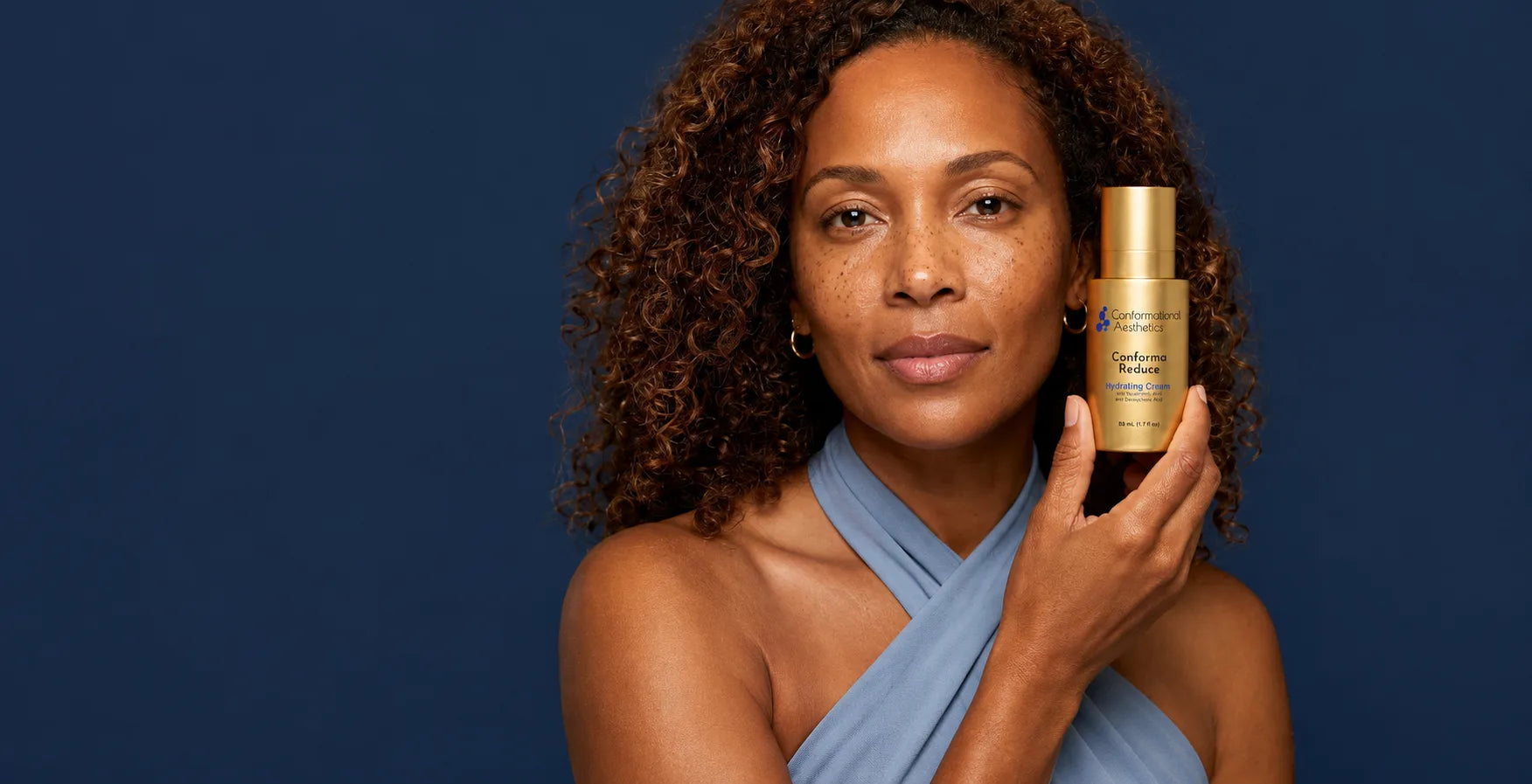 Woman holding a bottle of Conforma Reduce hydrating cream beside her jawline
