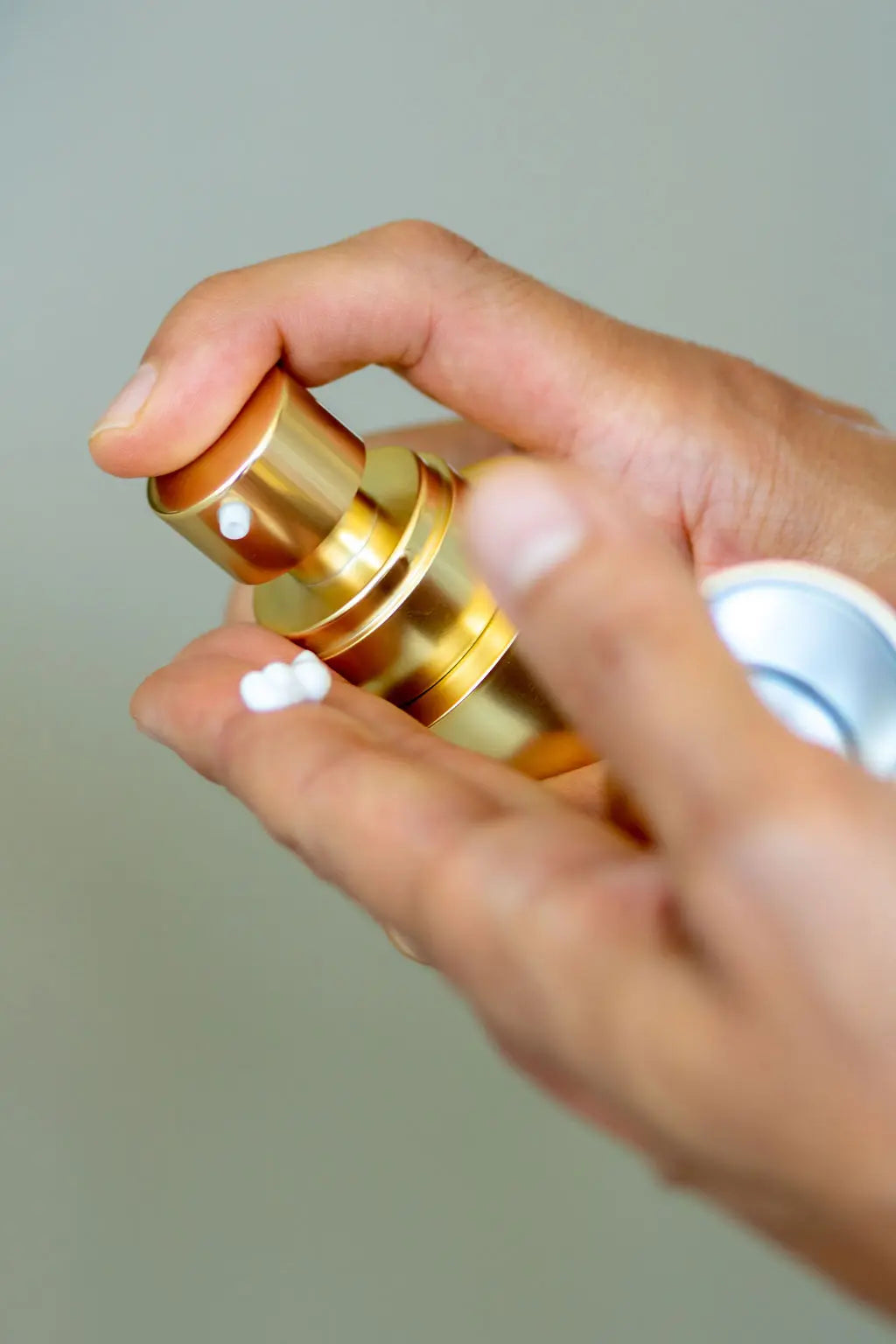 Close-up of a hand pressing a gold Conforma Reduce skincare pump and dispensing white cream onto a fingertip.