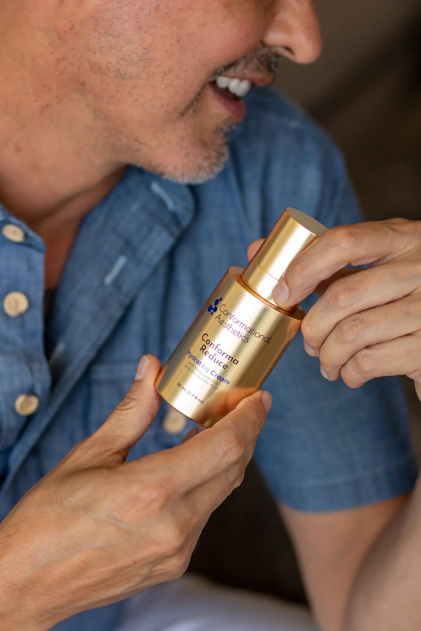 A close-up of a man holding a gold cosmetic bottle labeled 'Suncalmant' and 'Citronello Bioidentico' against a soft-focus background.